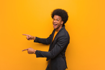 Young business african american man over an orange wall pointing to the side with finger