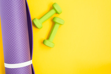 Yoga mat and dumbbells over yellow background, top view. Sport concept