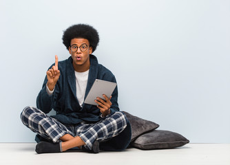 Young black man sitting on his house and holding his tablet having a great idea, concept of creativity