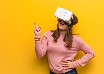 Young cute woman wearing a virtual reality googles pointing to the side with finger