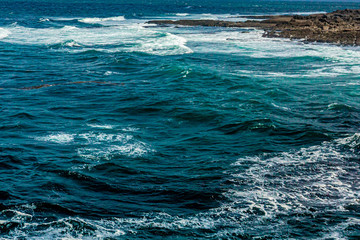 Choppy swells breaking on rocky hailite shoreline of Bothar nA, crystal clear turquoise blue water, spring day in County Clare in Ireland. Wild Atlantic Way