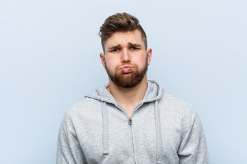 Fototapeta premium Young handsome fitness man blows cheeks, has tired expression. Facial expression concept.