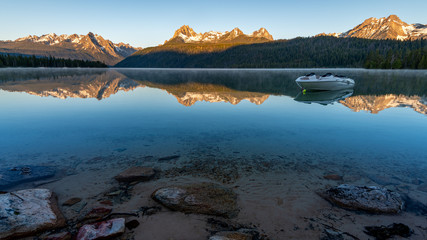 Boat floats on mountain lake amongst the reflection of peaks and forest