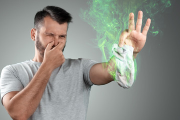 A young man holds his smelly socks and covers his nose with his hand. Nasty smell. Stink legs,...