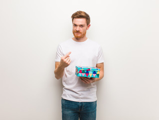 Young redhead man inviting to come. Holding a gift box.
