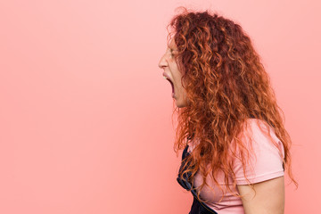 Obraz premium Young pretty ginger redhead woman wearing a jeans dungaree shouting towards a copy space