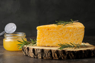 A piece of tasty marbled cheese on a wooden stand with rosemary and honey on a dark background.