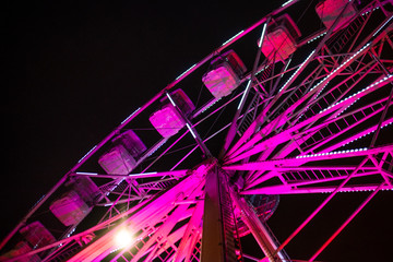 Close up of a bright pink ferris wheel lit up against a dark sky during a festival in a city