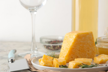 Slices of delicious marble cheese with a sprig of rosemary, honey and a cheese knife and white wine on a plate on a light concrete background.