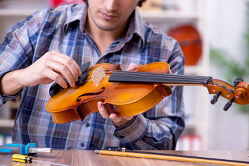 Young handsome repairman repairing violin