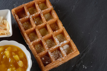 A large Viennese waffle cooked at home is on a black background and ready for filling fruit sauce