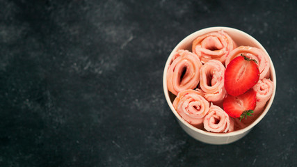 Rolled ice cream with strawberry in cone cup on dark background. Strawberry iced rolls top view or...