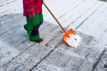 Child in snow pants and with gloves pushes snow with a slider