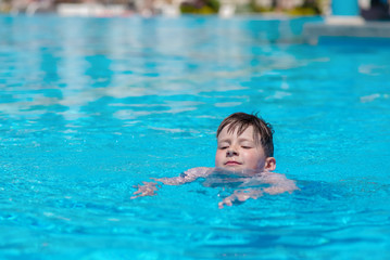 Fototapeta na wymiar Caucasian boy spending time in pool at resort. He is learning to swim..