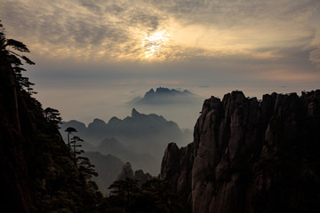 Tree silhouettes during sunset, Vibrant red and orange sky, mountains and horizon. Sanqing Mountain in Jiangxi Province, China. Mist and Fog in the distance, pine tree silhouettes.