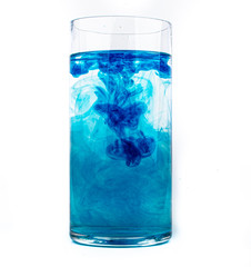 Blue food coloring diffuse in water inside glass with empty copyspace area for slogan or advertising text message, over isolated white background.