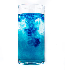Blue food coloring diffuse in water inside glass with empty copyspace area for slogan or advertising text message, over isolated white background.
