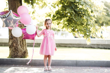 Naklejka premium Smiling baby girl 4-5 year old holding balloons outdoors. Looking at camera. Birthday party.