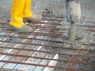 Construction worker pours concrete in yellow rubber boots with a hose for a foundation