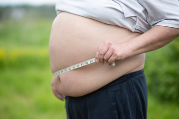 The fat man measures his stomach with a tape.