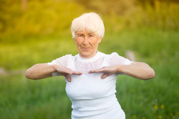 An elderly woman is engaged in fitness on the street in nature.