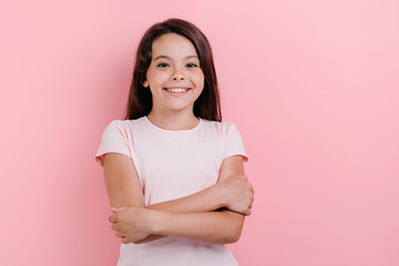 Little girl standing with folded her hands over pink background