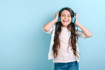 Portrait of a delightful little girl with closed eyes in earphones listening to music and sing touches her head - Image