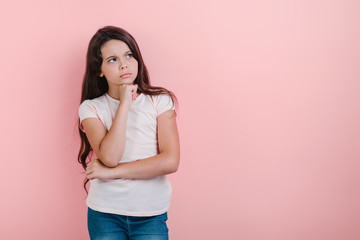 thoughtful young girl over pink studio background stands touches herself to chin. - Image