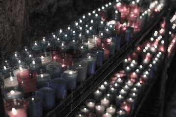 Desaturated closeup of colorful candles burning in the tunnel of Covadonga, Cangas de Onis, Asturias, Spain. Spirituality.