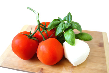 Tomatoes mozarella and basil salad ingredients on wooden board isolated on white background