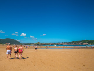 Senior people strolling along the beach in summer (Isla , Cantabria, Spain)