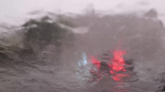Blurred car traffic and headlights through the heavy rain water drops on car window glass in rainy day with thunderstorm, bad summer weather.