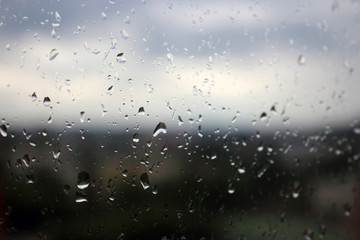 Big raindrops on window glass with blurred city view