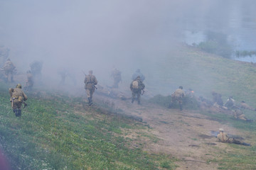 Soldiers in Soviet uniforms, with assault rifles, on the river bank, in the smoke