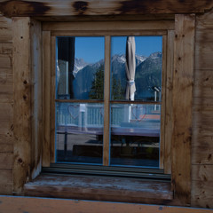 Holzfenster mit Spiegelung von Bänken und Bergen