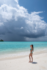 Fototapeta na wymiar A young girl in a turquoise swimsuit is standing on a white beach.