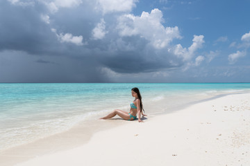 A young girl in a turquoise swimsuit is lying on a white beach.