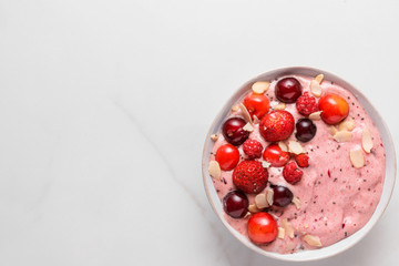 pink smoothie bowl with fresh berries, nuts and seeds on white marble table. healthy breakfast. top view