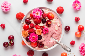 nice cream or smoothie bowl made of frozen bananas and berries with rose flowers, nuts and seeds...