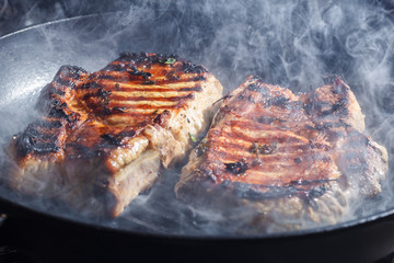 smoke and steam rise from a pork steak on grill pan.