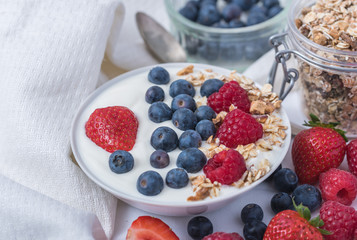 White yogurt in bowl with oatmeal and strawberries, blueberries and raspberries on the top on white background.