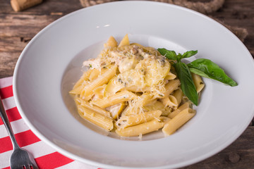 Delicious creamy Italian penne pasta starter with pepper seasoning and fresh basil on rustic wooden table