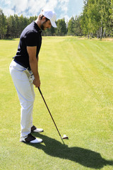 Fototapeta premium Full length of golf player playing golf on sunny day. Professional male golfer taking shot on golf course.