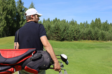 Golf player walking and carrying bag on course during summer game golfing.