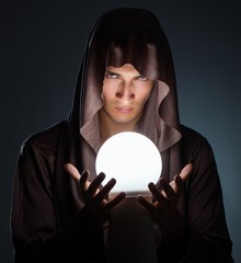 Young wizard with crystal ball in dark room