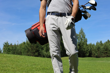 Cropped image of male golfer carrying golf bag with drivers while walking by green grass.