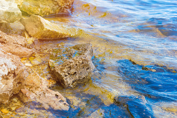 Stone near the river. Waves run on the coastline. Summer sunset. The sun's rays are reflected in the water.