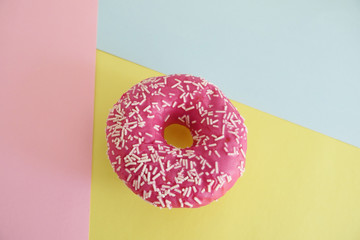 Juicy Pink Sprinkled Donut isolated on a Geometric Pink, Blue and Yellow Background