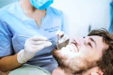 Giovane ragazza dentista sta visitando un paziente ragazzo con barba sulla poltrona.