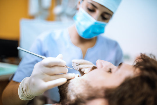 Giovane ragazza dentista sta visitando un paziente ragazzo con barba sulla poltrona.
